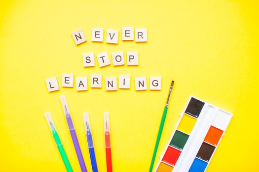 Words from wooden blocks "never stop learning" and stationery on bright yellow background