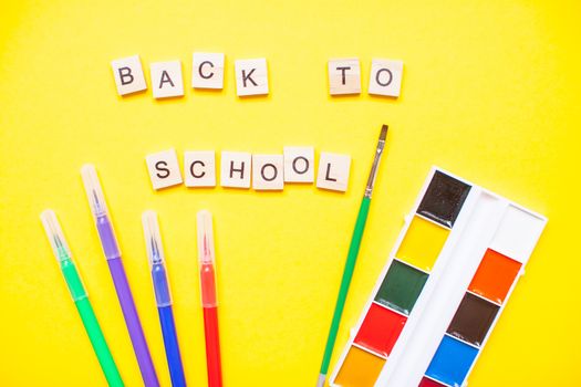 Words from wooden blocks "back to school" and stationery on bright yellow background