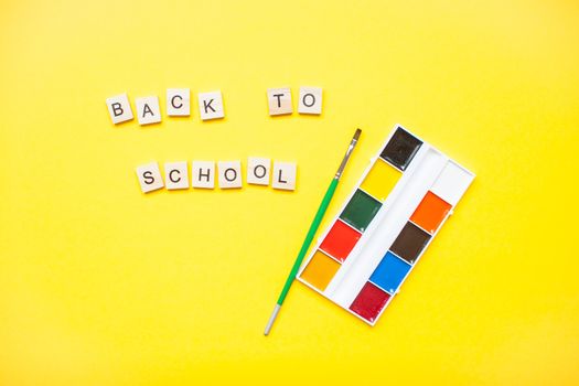 Words from wooden blocks "back to school" and stationery on bright yellow background