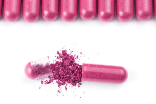 row of plastic pink color organic capsules isolated on white background closeup with one opened.