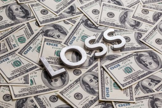 a word loss laid by metal letters on dollar banknotes background.