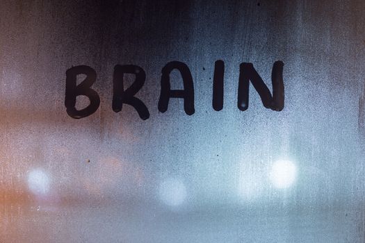 the word brain written on night wet window glass close-up with blurred background.