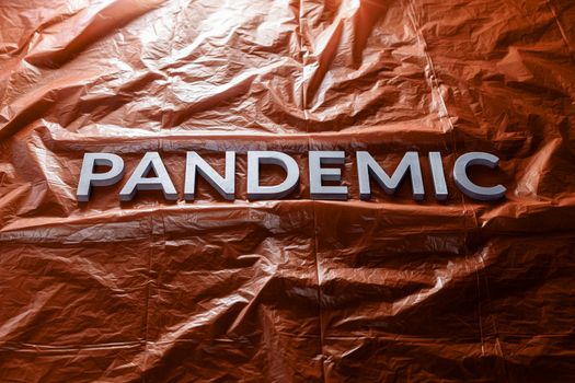 The word pandemic laid with silver letters on red crumpled plastic film background Slanted centered with dramatic ight.