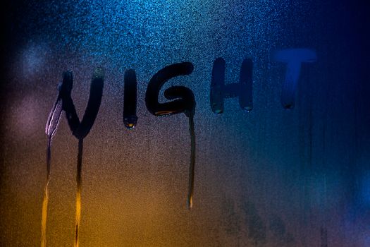 the word NIGHT written on nightime wet window glass close-up with blurred background.
