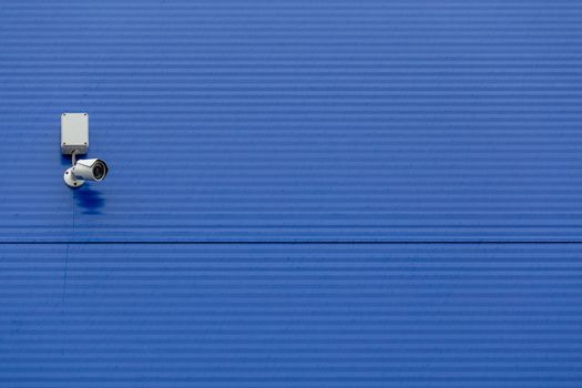 small white security camera on large blue steel silo wall.