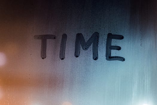 the word time handwritten by finger on night wet window glass.