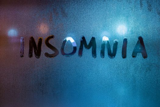the word insomnia written on night wet window glass close-up with blurred background.
