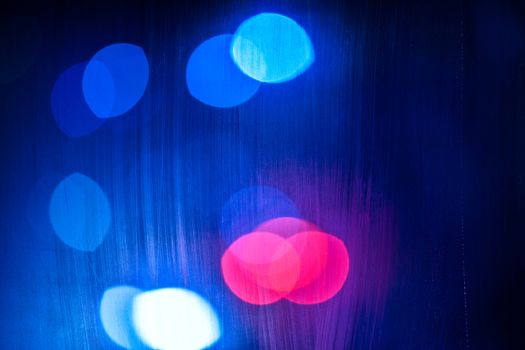 an abstract background of red, purple and blue night street lights bokeh trough wet glass with selective focus.
