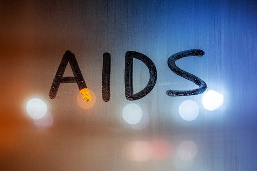 the word AIDS written on night wet window glass close-up with bokeh background.