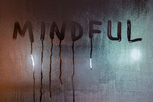 the word mindful written on night wet window glass close-up with blurred background.