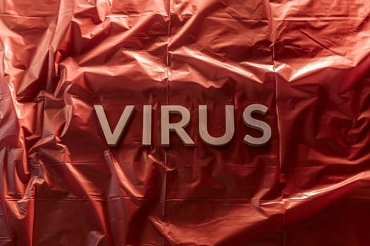 the word virus laid with brushed silver metal letters on red background of crumpled plastic film in horizontal centered composition and dramatic light