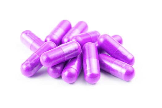 pile of proton purple color organic capsules isolated on white background closeup with selective focus.