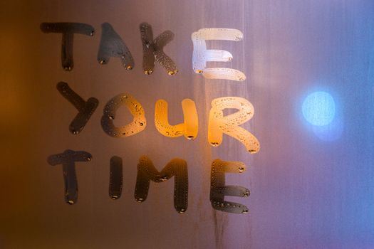 the phrase take your time written by finger on night wet glass with blurred street lights, close-up with selective focus.