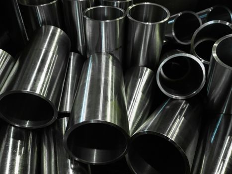 dark industrial background with cnc machined shiny steel pipes - selective focus and lens blur technique