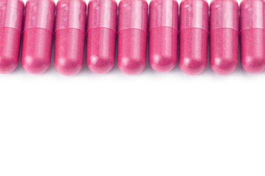 row of plastic pink color organic capsules isolated on white background closeup with selective focus.
