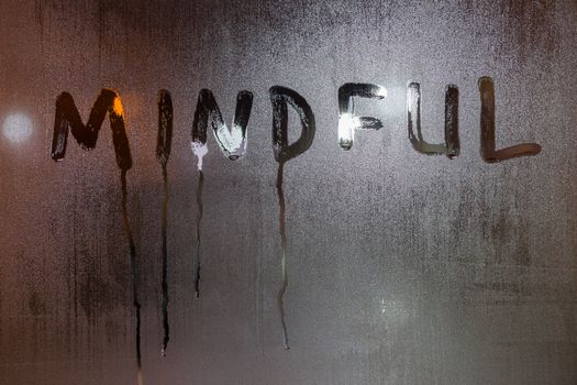 the word mindful written on night wet window glass close-up with blurred background.