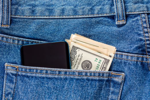 US dollar banknotes and smartphone in the left rear pocket of blue jeans. Concept of saving money or pocket expenses.