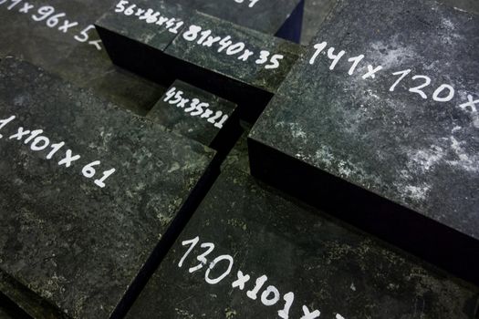Raw steel bricks after thermal hardening with black slag. Selective focus technique. White numbers - dimensions in mm.