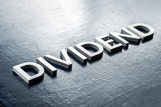 the word dividend laid by silver metal letters on gloss painted board background with selective focus in diagonal perspective