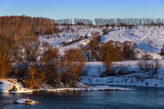 amateur winter riverside landscape with birch forest and slope.