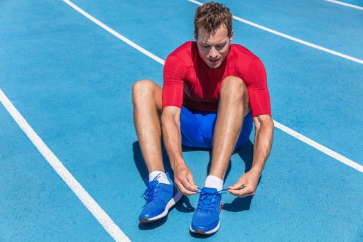 Athlete sprinter getting ready to run tying up shoe laces on stadium running tracks. Man runner preparing for cardio training outdoors. Fitness and sports.