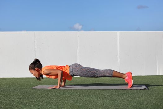 Yoga fitness woman practicing chaturanga pose push ups or press up on exercise mat at outdoor home. Fit and healthy young girl doing morning core body workout push up strength training.