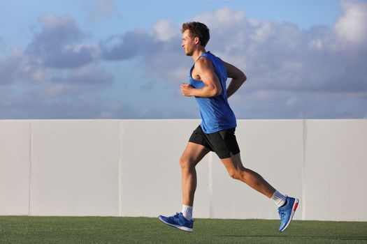 Young man runner running in city park on summer grass outdoors at sunset at outdoor stadium fitness centre. Healthy lifestyle.