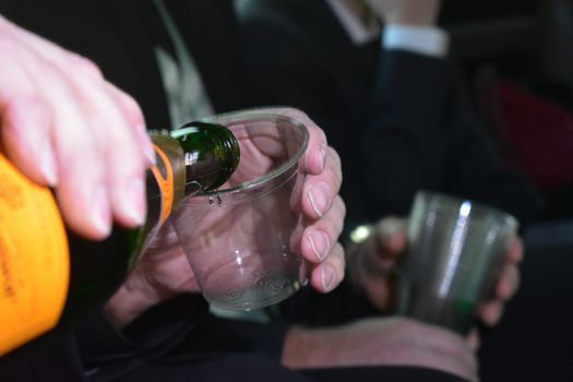 A Man in a Suit Pouring an Alcoholic Beverage Into a Clear Plastic Cup