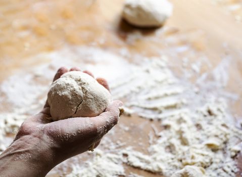 a female hand holds a flour dough with a wooden board dirty with flour in the background. Kneading and preparing bread, pizza and pasta. Raw food.