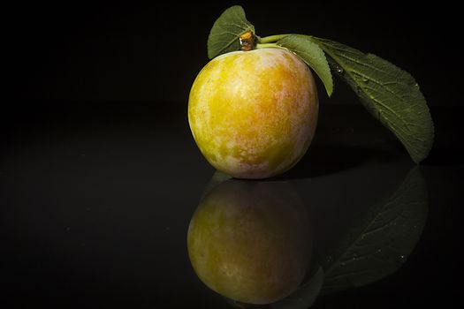 Ripe plums on a black reflective surface
