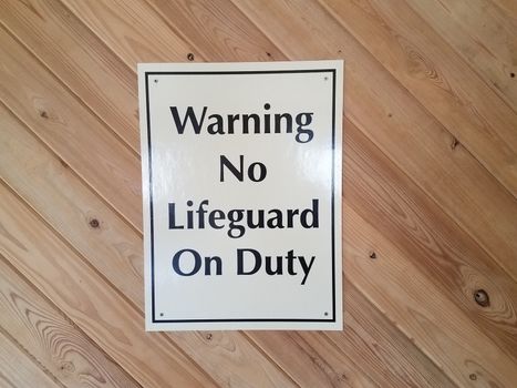 white warning no lifeguard on duty sign on wood wall