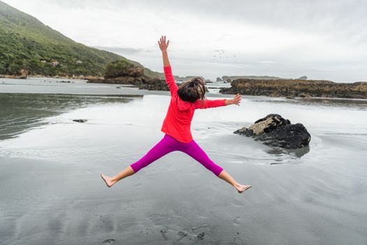 Carefree happy girl jumping of fun on beach - Woman enjoying outdoor life doing star jump on holiday travel.