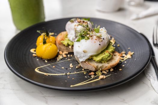 Avocado toast with eggs breakfast plate at restaurant closeup. Trendy healthy morning food at cafe with guacamole and poached egg top view.