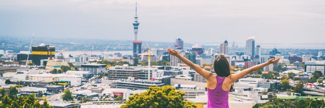 Auckland city skyline view from Mount Eden banner. Sky tower, New Zealand. Happy woman with arms up in freedom and happiness at top of Mt Eden urban park famous tourist attraction.