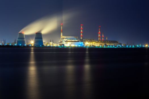 old thermal 450 megawatt power plant at night with artificial lake on foreground.