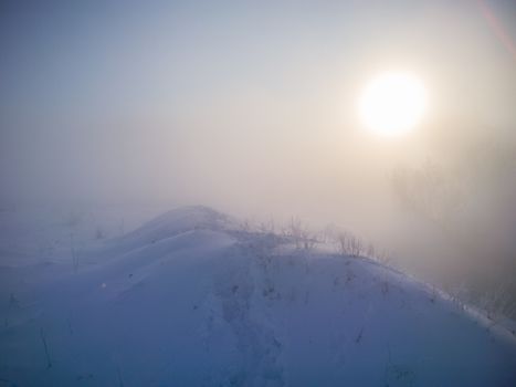 winter snow hill with footprints in deep snow at foggy morning.