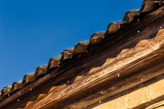 spring water drops flying from edge of an old barn roof.