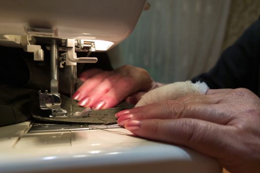 a hand of aged womans with a bandaged finger sews with a sewing machine - close-up with selective focus