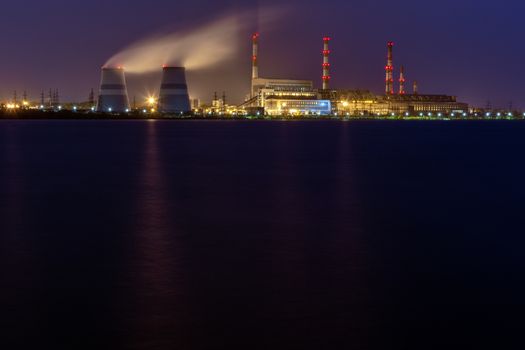 old thermal 450 megawatt power plant at night with artificial lake on foreground.