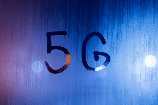 the word 5G written by finger on wet glass with blurred lights in background.