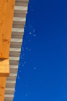 spring water drops flying from edge of barn roof with selective focus.