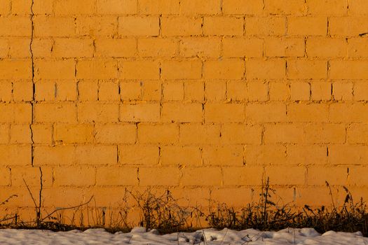orange plaster rough brick wall texture under direct sunlight with snow and dry gasss under
