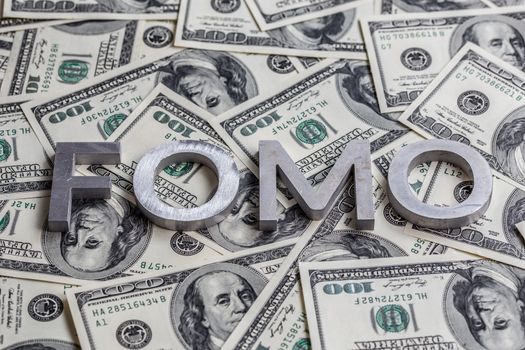 The word FOMO - fear of missing out - laid with aluminium letters on the US dollar banknotes background - with selective focus.