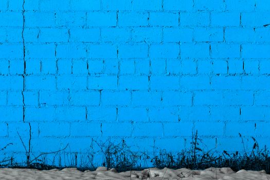 blue plaster rough brick wall texture under direct sunlight with snow and dry gasss under