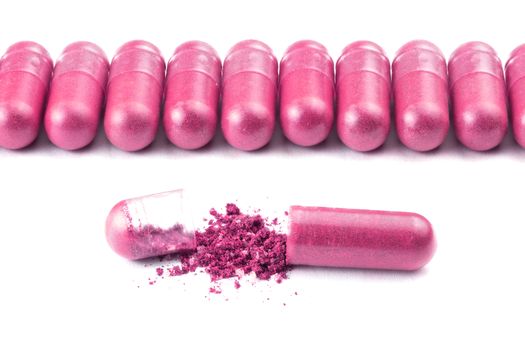row of plastic pink color organic capsules isolated on white background closeup with one opened.