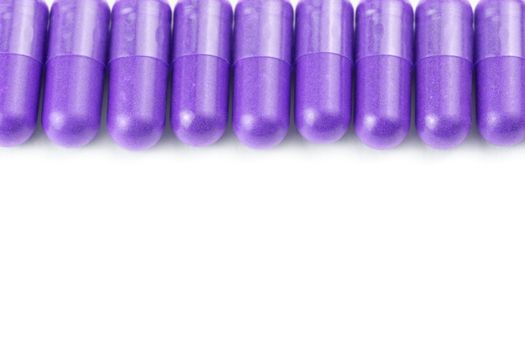 row of proton purple color organic capsules isolated on white background closeup with selective focus.