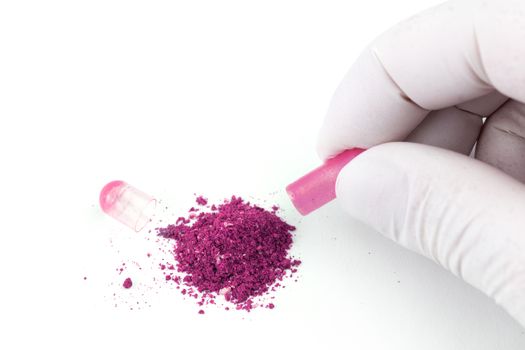 hand in medical glove opening plastic pink color organic med capsule isolated on white background closeup.