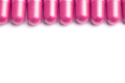 row of plastic pink color organic capsules isolated on white background closeup with selective focus.