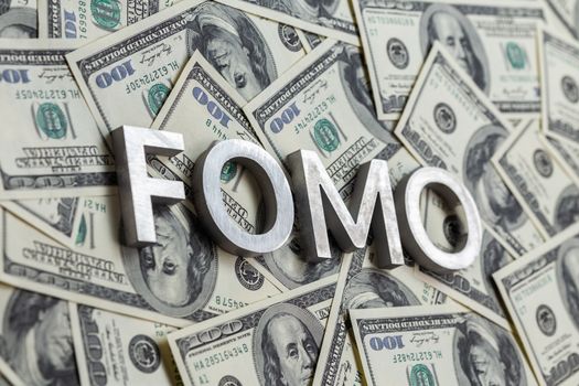 The word FOMO - fear of missing out - laid with aluminium letters on the US dollar banknotes background - with selective focus and diagonal composition.