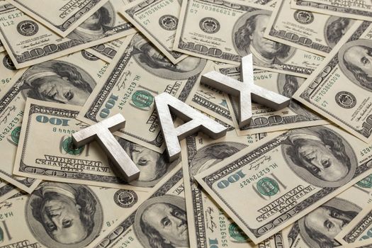 The words TAX laid with aluminium thick letters on the US dollar bills background - with selective focus and diagonal composition.
